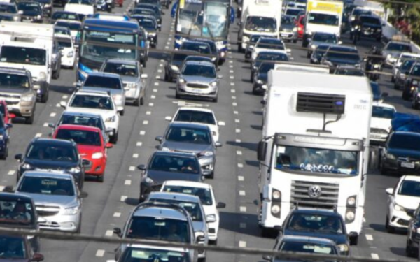 Trânsito intenso com carros e caminhões em rodovia movimentada durante horário de pico.